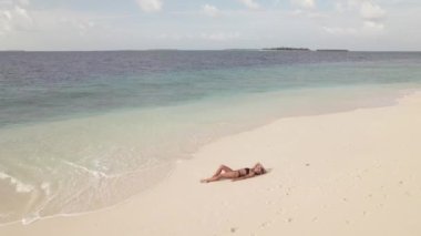 Kumlu sahilde uzanmış, okyanus dalgaları vücuduna sıçrayan bir kadının insansız hava aracı görüntüsü. Tropik plajlardan, tatil beldelerinden ve tatillerden geri dön. Seyahat ve seyahat kavramı