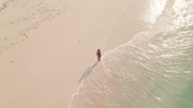 Tropikal plajda yürüyen kızın turkuaz deniz dalgaları kıyıya vururken hava görüntüsü. Maldivler, Hint Okyanusu. Tatil ve seyahat. Yüksek kalite 4k görüntü