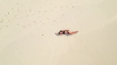 Drone uzaklaştı, kumlu sahilde uzanan kadının en üst görüntüsü, vücuduna okyanus dalgaları sıçrıyor. Tropik plajlardan, tatil beldelerinden ve tatillerden geri dön. Seyahat ve seyahat kavramı