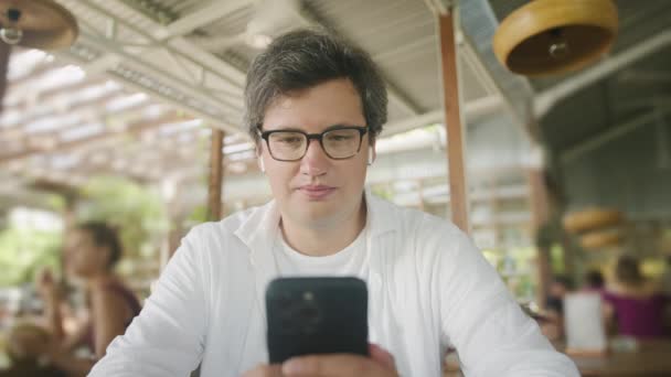カフェのテーブルに座っている間 インターネットの閲覧 テキストメッセージのためにスマートフォンを使用してビジネスフリーランスの男 ライフスタイル コーヒーショップのコンセプトで働く ソーシャルメディア — ストック動画