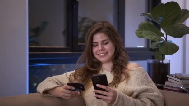 Sorrindo Jovem Cliente Segurando Cartão Crédito Smartphone Sentado Sofá Casa — Vídeo de Stock