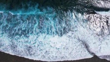 Yukarıdan dalgalar geliyor. Mavi turkuaz okyanusta 4K drone görüntüsü, yavaş çekim. Büyük dalgalar sahil şeridini vurdu. Bali, Endonezya.