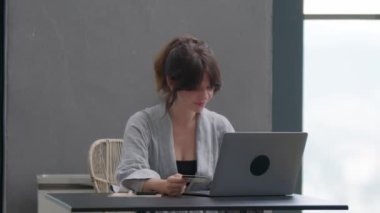 Odaklanmış iş kadını girişimci dizüstü bilgisayar ve kredi kartıyla online ödeme yapıyor. Evden sanal bir pazar yerinden kıyafet alan genç bir kadın. Yüksek kalite 4k görüntü