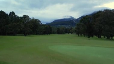 Yeşil golf sahası, tropikal orman ve çayır üzerinde insansız hava aracı görüntüsü. Bulutlu gökyüzünün, güzel doğanın ve dağların altındaki manzaralı Bali manzarasına zum yap. Ekonomik seyahat kavramı