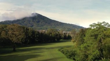 Dağa yakın evleri olan golf sahasının ve köyün insansız hava aracı görüntüsü. Bali doğası, yeşil ağaçlar ve ormanlı tarla. Seyahat ve Endonezya 'ya tatil gezisi kavramı