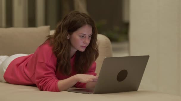 Mooie Jonge Vrouw Roze Sweatshirt Liggend Bank Sms Laptop Gezellig — Stockvideo