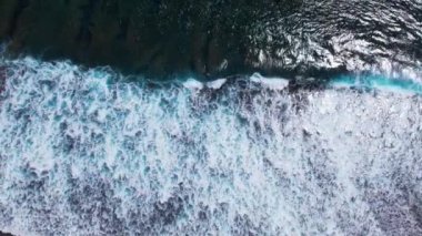 Hava dalgaları sağdan sola, köpüklü okyanus dalgaları kıyıya vuruyor. Sandy Beach 'in yavaş çekim drone görüntüsü. Kuş bakışı deniz kıyısına çarpan deniz suyu manzarası