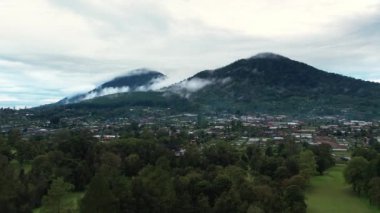 Bali manzarası ve kırsal köy üzerinde, bulutlu gökyüzünün altında göl ve dağ manzaralı hava aracı ağır çekim. Endonezya manzarasının panoramik görüntüsü