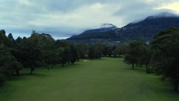 フィールドの近くに家を持つゴルフコースと村の空中ビュー レクリエーションと休日の場所 山と曇りの空を撮影したドローン 島へ旅行するコンセプト — ストック動画