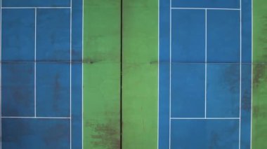 İki tenis kortunun üzerinde uçan, yeşil palmiye ağaçları ve evlerle çevrili bir hava aracı. Açık hava sporu, eğlence ve eğitim için yeşil alan manzarası