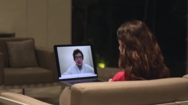 İnternette video konferansı yapan bir kadın, bir erkekle konuşan bir laptop ekranı. Şutun üzerinde, kanepe ile iç mekan. Sanal görüşme ve röportaj kavramı