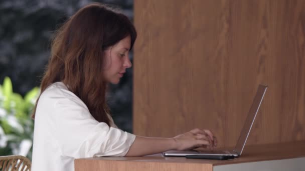 在笔记本电脑 侧视木制吧台台面上打字时 微笑的女性形象 与朋友或同事在线聊天 远程工作 通信和自由职业的概念 — 图库视频影像