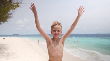 Mutlu beyaz çocuk atlıyor ve el sallıyor yaz tatili boyunca plajda selam vermek için, video portresi. Yüksek kalite 4k görüntü