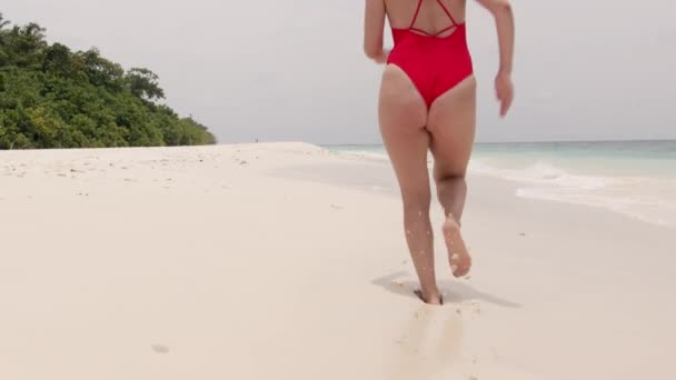 モルディブの海岸線に沿ってジョギングする赤い水着の若いフィットウーマン スローモーションショット ライフスタイル 女の子はインド洋の砂の上にビーチで走ります 高品質の4K映像 — ストック動画