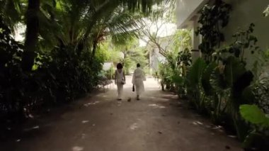 Beyaz gelinlik giymiş iki güzel kadın köyde ve Maldivler 'deki tropikal orman adasında sahile doğru yürüyorlar. Tatil ve seyahat kavramı
