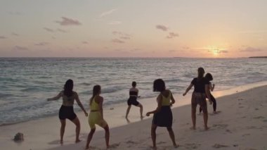 Bir grup profesyonel dansçı gün batımında Maldivian plajında prova yapıyorlar. Hava aracı üstgeçitten ateş etti. Yüksek kalite ağır çekim 4k görüntü.