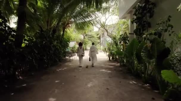 两个身穿白色婚纱的漂亮女人正穿过马尔代夫的村庄和热带丛林岛走向海滩 假日和旅行的概念 — 图库视频影像