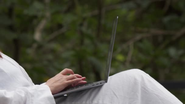 テラスのノートパソコンを使った白いバスローブの女性 バックグラウンドのジャングル クローズアップショット 距離作業の概念 — ストック動画