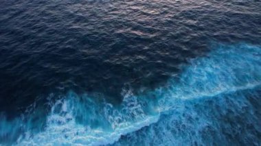 Düşen okyanus dalgalarının yukarıdan aşağıya doğru görüntüsü, İHA gün batımında derin suyun üzerinde yavaşça havada süzülüyor. Gili Trawangan Adası, Lombok. Yüksek kalite 4k görüntü