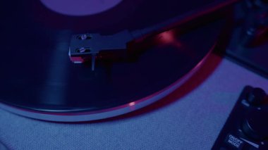 Üst görüntüler, bir vinil plak çalara sanatsal bir yaklaşım sergileniyor, modern ortamlarda müzik ve yaratıcılığın havasını yükselten çevre ışıklarıyla aydınlatılıyor..