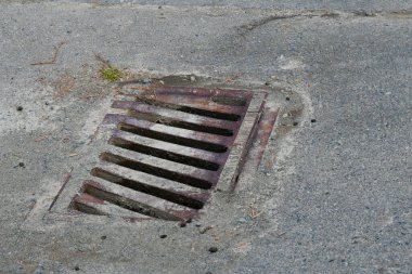 Asfaltlı bir yolda paslanmış eski bir metal rögar..