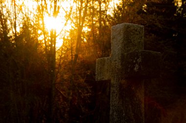 Akşamın geç saatlerinde gün batımında altın ışıkta geçen tek bir taş haçın görüntüsü..  