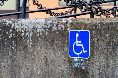 A blue and white wheelchair accessible parking sign posted on a concrete wall. 
