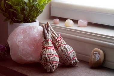 A close up image of a large raw piece of rose quartz with two white sage smudge sticks.  