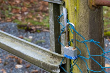 A close up image of a gate which has been locked by an old blue metal padlock.  