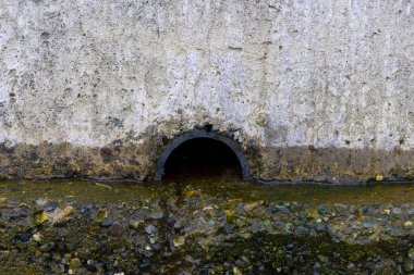 An image of an open water drain built into a concrete wall.  