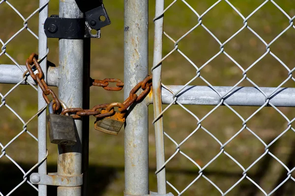 A close up image of a metal gate locked with a black padlock and rusted chain.