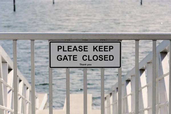 stock image An image of a white metal gate and warning sign on a boat launch ramp. 