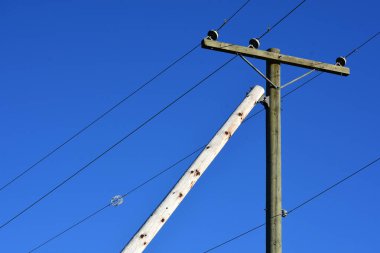 Açık mavi gökyüzüne karşı tek bir uzun elektrik direğinin ve iletim hatlarının görüntüsü..