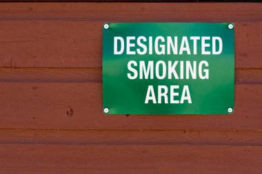 Kahverengi bir duvarda yeşil bir sigara içme alanı tabelası.. 