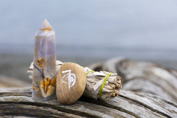 An image of a healing reiki symbol with white sage smudge stick and crystal tower on an old weathered driftwood log. 