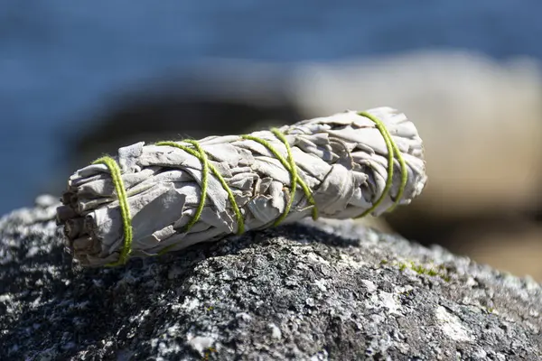 明るい緑の糸で覆われた岩の上に眠る白いセージのスモッジスティックのイメージ ストックフォト