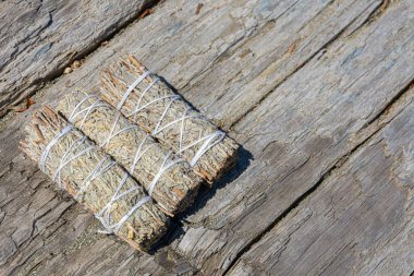 A close up image of three healing smudge sticks on a sun bleached driftwood log.  clipart