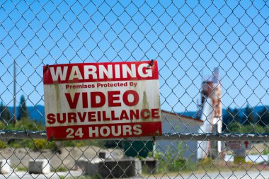 A close up image of a very old video surveillance warning sign posted on a locked chain link gate.  clipart