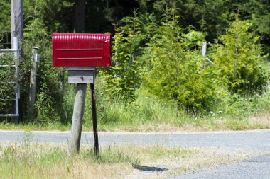 Kırsal bir yolun kenarında parlak kırmızı bir posta kutusunun resmi.. 