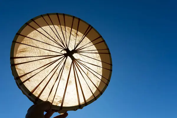 Stock image An image of a handmade leather meditation drum being held up against a bright blue sky. 