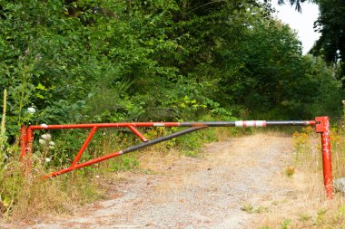 Kırsal bir yola erişimi kısıtlayan kapalı bir kırmızı metal kapının görüntüsü.. 