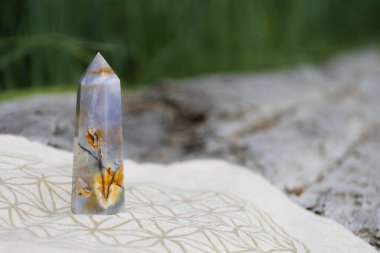 A close up image of a blue lace agate tower on a grid cloth with the flower of life pattern.  clipart