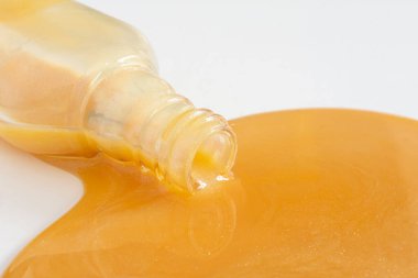 Beyaz arka planda dökülen altın renkli tırnak cilası şişesinin yakın plan görüntüsü.. 