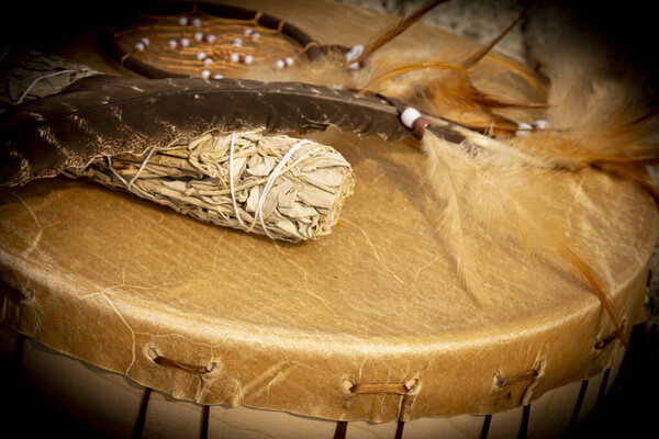 A close up image of a hand made leather meditation drum with white sage and dream catcher.