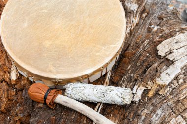 A close up image of a handmade leather meditation drum with white sage smudge stick and rattle. clipart