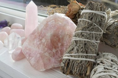 Kurutulmuş gül ve kurdeleyle süslenmiş dekoratif beyaz adaçayı lekesi. Yanında birkaç parlak kuvars kristali ve kuvars kulesi var..