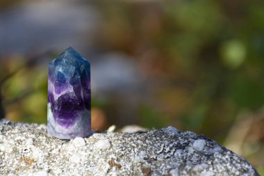 A close up image of a tiny fluorite crystal tower resting on a rock and sparkling in the sunlight.  clipart