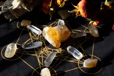 Citrine crystal, recognized for its warm yellow hue, serves as the centerpiece of a healing grid. Surrounding it, clear quartz crystals are meticulously arranged on a black cloth adorned with an intricate golden geometric pattern. 