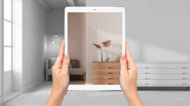 Hands holding tablet showing living room in japandi style, total blank project background, augmented reality concept, application to simulate furniture and interior design products