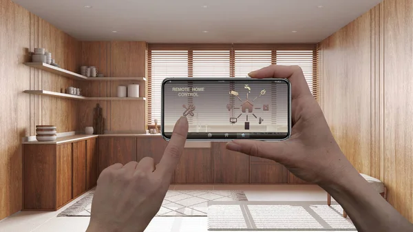 Remote home control system on a digital smart phone tablet. Device with app icons. Interior of japandi wooden kitchen in the background, architecture design